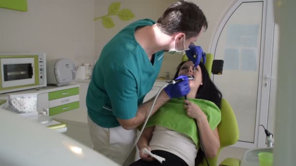Mladý pohledný zubař opravuje zuby pacientka.