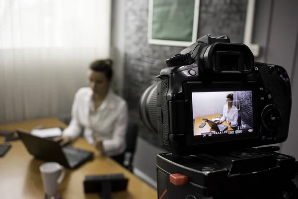 Video camera shoots a young businesswoman sitting at a table in front of a laptop