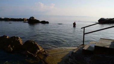 Bir erkekte geç öğleden sonra boyunca taşlarla çevrili deniz 