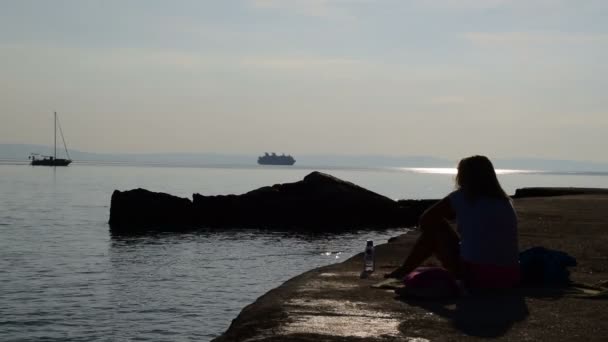 Silhouet Van Een Meisje Zittend Het Strand Kijken Een Zeilboten — Stockvideo