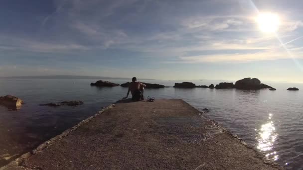 男は分割の海岸に座っているし 海を見て — ストック動画