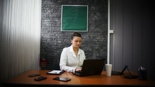 ノート パソコンの前に白いスーツのビジネス女性がコーヒーを飲む — ストック動画