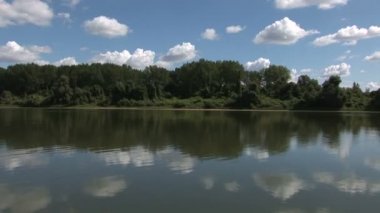 Nehir orman, mavi gökyüzü ve beyaz bulutlar güneşli bir günde çevrilidir