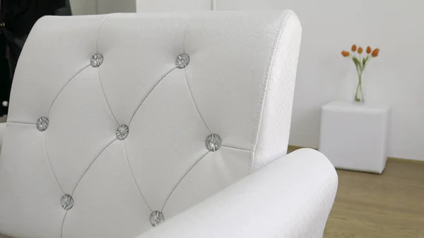 The back of the white leather armchairs with diamonds - Bouquet of orange tulips in the background.