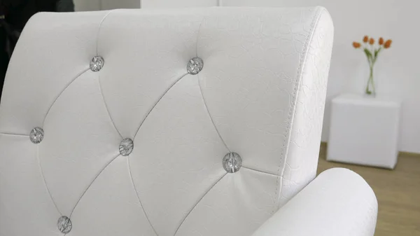 The back of the white leather armchairs with diamonds - Bouquet of orange tulips in the background.