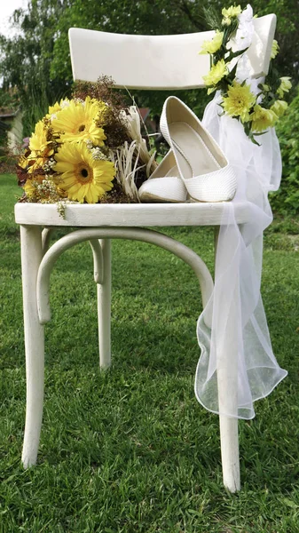 黄色のガーベラデイジーの花束 花嫁の白い靴と緑の庭の白い木製の椅子のベール — ストック写真