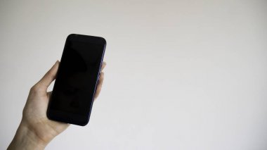 Bir kadının sol eli beyaz bir arka plan üzerinde boş siyah telefon tutar