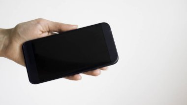 Beyaz kadın sol el ile beyaz bir arka plan üzerinde siyah bir cep telefonu tutar