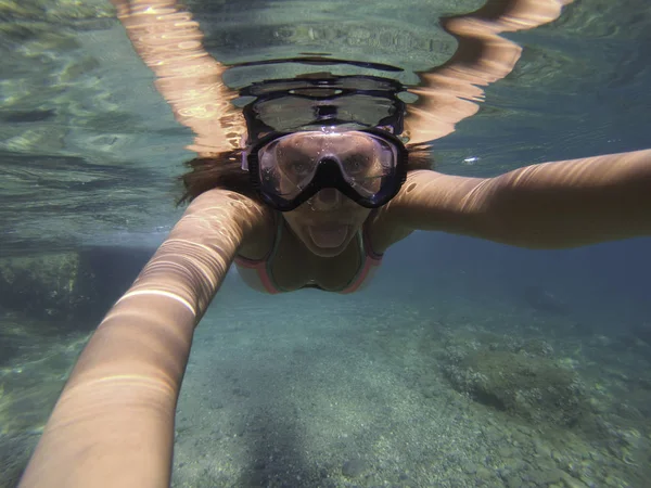 A woman with a diving mask under water showing her tongue to the camera
