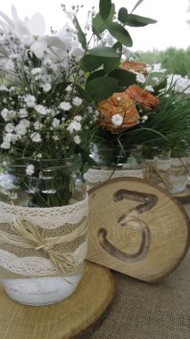 Kavanozlarda beyaz papatya çiçekleri ve turuncu güllerle süslenmiş üç numaralı masa