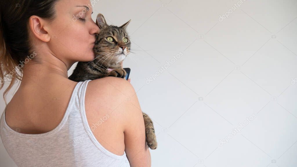 Caucasian woman hugs and kisses the striped cat. Negative space. Copy space for text.