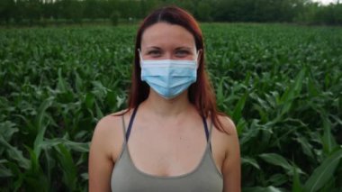 Mısır tarlasında duran tıbbi maskeli bir kadın iki eliyle baş parmağını kaldırıyor..