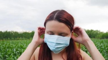 Agronomist çiftçi kadın yüzüne koruyucu bir maske takar ve mısır tarlasına ve kameraya bakar..