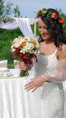 Bir bütçe ve düğün masasının önünde başında çiçek çelengi olan gülümseyen gelin. Mutlu gelin buketine bakar..