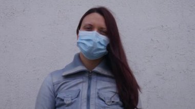 Coronavirus salgını sırasında beyaz bir duvarın önünde cerrahi maske takan bir kadının portresi..
