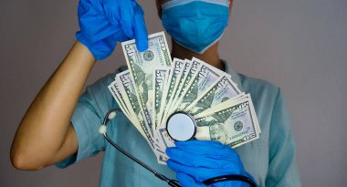Sağlık sigortası ve sağlık sigortası konsepti. Tıbbi maskeli, eldivenli ve steteskoplu bir kadın doktor parayı elinde tutuyor..