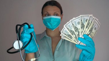 Koruyucu maskeli ve eldivenli bir kadın doktor bir elinde stetoskop, diğerinde para tutuyor. Meslek ve yolsuzluk arasındaki seçim.