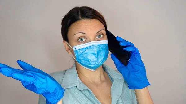 Woman doctor or nurse with face mask and latex gloves talking on phone.