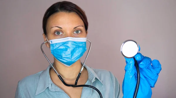 Portrait of a doctor woman with a stethoscope. Nurse in a blue uniform, protective mask and latex gloves.