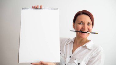 Beyaz kadın elinde boş bir bez tutuyordu ve ağzında bir boya fırçası vardı..