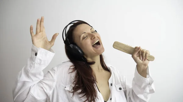 女人通过她的立体声耳机听音乐 并假装用实际上是梳子的话筒唱歌 — 图库照片
