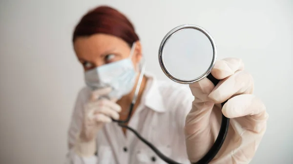 A female doctor performs an examination with a stethoscope. Concerned doctor with focus on her hand and stethoscope.