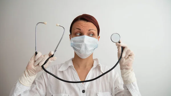 Indoor shot of medical worker. Woman wearing white shirt, rubber gloves and medical mask. The doctor holds a stethoscope on a white background. Negative space or copy space for text.
