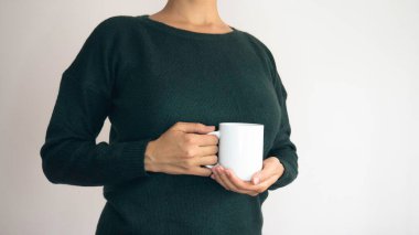 Elinde beyaz bir fincan çay ya da kahve tutan yeşil kazaklı bir kadın. Metin için boşluk kopyalama alanı negatif.