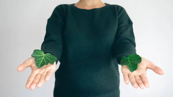 A woman in a green sweater with a green creeper leaf in her hands.