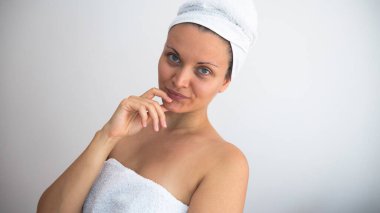 Banyo yaptıktan sonra beyaz havluya sarılı makyajsız bir kadın doğrudan kameraya bakar..
