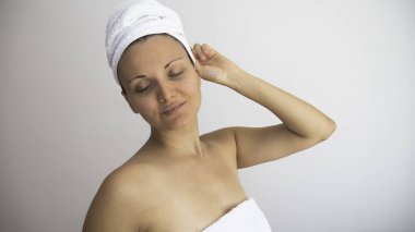 Gözleri kapalı, başı ve vücudu beyaz arka planda temiz beyaz havlulara sarılmış bir kadın. Metin için negatif boşluk veya kopyalama alanı.