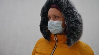 Rüzgârda sarı ceketli bir kadının portresi. Tıbbi maskesini çıkarıp havayı soluyor. Sonra kameraya bakıyor ve maskesini tekrar yüzüne takıyor..