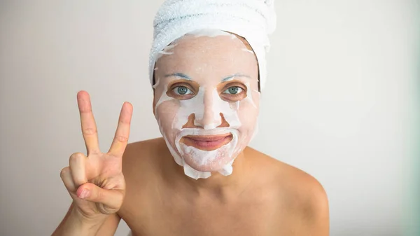 Kobieta Owinięta Biały Ręcznik Maską Kosmetyczną Daje Znak Zwycięstwa Lub — Zdjęcie stockowe