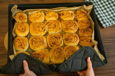 Elleri taze pişmiş tarçınlı çörek tepsisi tutuyordu. Ev yapımı hamur işi sürecinin son aşaması.