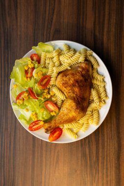 Kızarmış tavuk budu, salata ve sebzeli makarna.