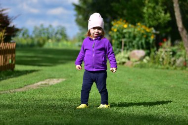 Mor ceketli, pembe şapkalı ve sarı ayakkabılı küçük bir kız güneşli bir günde kırsal alanda yürüyor. Kırsal alanda gezen sevimli bir çocuk..
