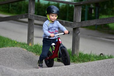 Kask takan genç çocuk yüksek kaldırımlı açık hava pompa pistinde kırmızı dengeli bisiklete biniyor. Yeşil park ortamında heyecan verici çocukluk sporları ve aktif oyun zamanı.