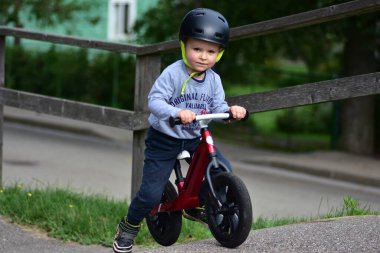 Kask takan genç çocuk yüksek kaldırımlı açık hava pompa pistinde kırmızı dengeli bisiklete biniyor. Yeşil park ortamında heyecan verici çocukluk sporları ve aktif oyun zamanı.