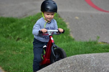 Kask takan genç çocuk yüksek kaldırımlı açık hava pompa pistinde kırmızı dengeli bisiklete biniyor. Yeşil park ortamında heyecan verici çocukluk sporları ve aktif oyun zamanı.