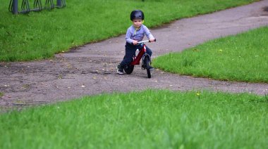 Kask takan genç çocuk yüksek kaldırımlı açık hava pompa pistinde kırmızı dengeli bisiklete biniyor. Yeşil park ortamında heyecan verici çocukluk sporları ve aktif oyun zamanı.
