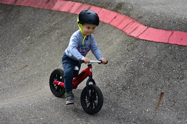 Kask takan genç çocuk yüksek kaldırımlı açık hava pompa pistinde kırmızı dengeli bisiklete biniyor. Yeşil park ortamında heyecan verici çocukluk sporları ve aktif oyun zamanı.