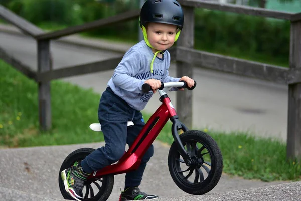 Kask takan genç çocuk yüksek kaldırımlı açık hava pompa pistinde kırmızı dengeli bisiklete biniyor. Yeşil park ortamında heyecan verici çocukluk sporları ve aktif oyun zamanı.