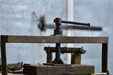 Kullanımı ve vidası olan paslı metal baskı aracı, mekanik çalışmayı, atölye atmosferini ve retro mühendislik tarihini sembolize eden endüstriyel miras nesnesi.