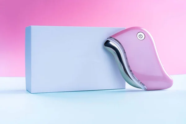 guasha device ultrasonic massage pink on a blue background is a bright color for a cosmetologist