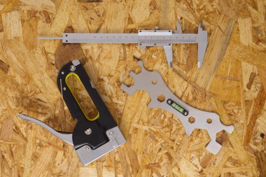 A variety of used tools on an OSB plywood background construction stapler, caliper, bubble level tool