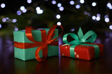 A gift box with a ribbon placed on a brown table, set against a backdrop of a pine branch decorated with twinkling fairy lights.