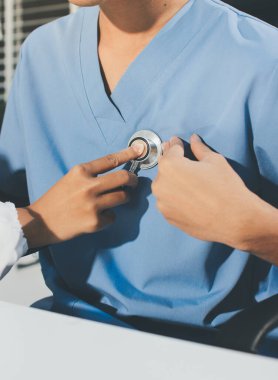 Bir doktor klinik randevusu sırasında hastanın kalbini incelemek için steteskop kullanır..