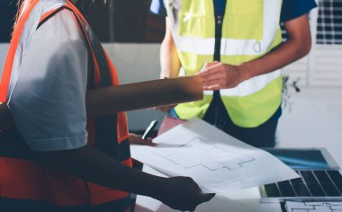 Endüstriyel mühendislerden oluşan bir ekip, fabrikadaki masada bulunan makine planlarını analiz ediyor. Fabrikada ya da üretim tesisinde çalışıyorum..