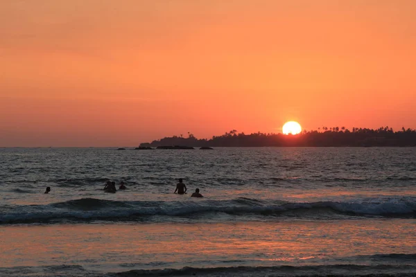 sunset on Weligama Bay Beach with silhouette people in the sea, Sri Lanka