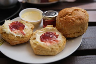Taze pişmiş çörekler pıhtılaşmış krema ve ahşap masada çilek reçeli ile servis edilir..